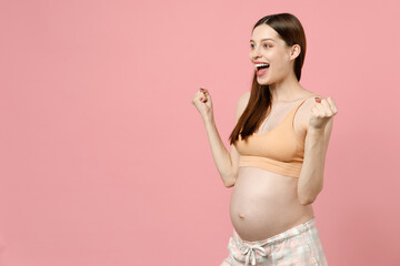Pregnant woman future mom in basic top with belly tummy with baby doing winner gesture say Yes clenching fists isolated on pastel pink background studio. Maternity family pregnancy gynecology concept.