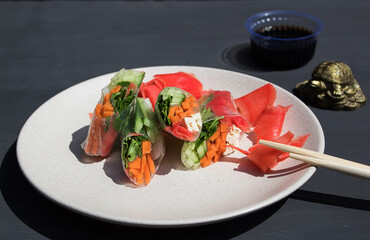 Spring or summer rolls of rice paper, carrots, cucumbers, ginger with sauce on gray background