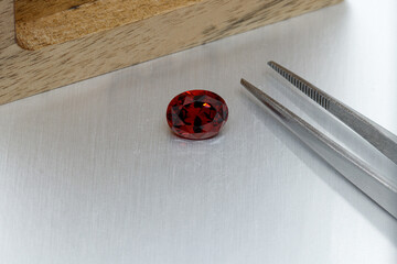 macro mineral faceted stone Garnet with tweezers on a gray background