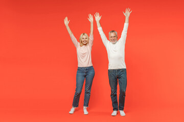 Fototapeta premium Full length of funny cheerful couple two friends elderly gray-haired man blonde woman in white pink casual clothes standing rising spreading hands isolated on orange color background studio portrait.