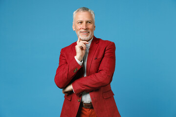 Smiling pensive elderly gray-haired mustache bearded business man wearing red jacket suit standing put hand prop up on chin looking aside isolated on blue color wall background studio portrait.