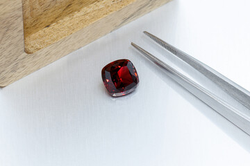 macro mineral faceted stone Garnet with tweezers on a gray background
