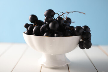 black grapes in a white bowl on a blue background