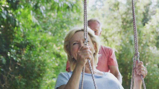 Retired senior couple having fun with man pushing woman on garden swing - shot in slow motion