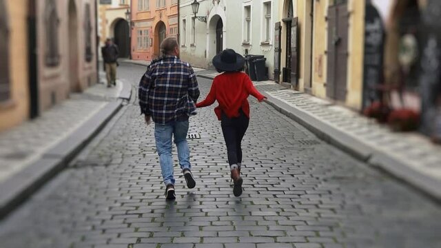 Sweet couple have romantic time while honeymoon trip in old european town. Young lovers holding hands running on street and kissing.