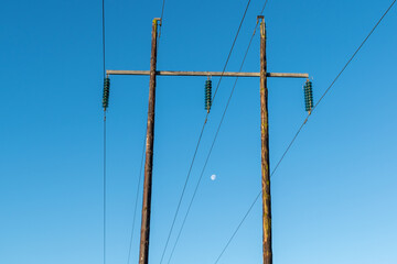 High voltage electricity power lines on blue sky with visible moon .