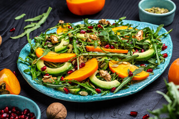 healthy delicious salad with persimmon slices, arugula, avocado, pumpkin seeds, walnuts, pomegranate, Healthy food. top view