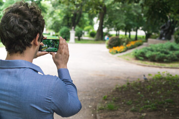 young man taking a photo of city park with his android phone