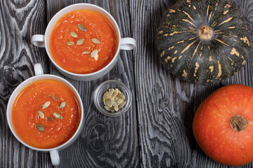 Pumpkin tomato cream soup. With the addition of pumpkin seeds. Several pumpkins are nearby. View from above. On pine boards.