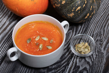 Pumpkin tomato cream soup. With the addition of pumpkin seeds. Several pumpkins are nearby. On pine boards.