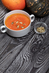 Pumpkin tomato cream soup. With the addition of pumpkin seeds. Several pumpkins are nearby. On pine boards.