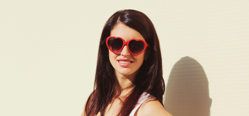 Close up portrait of young woman wearing a red heart shaped sunglasses over a white background