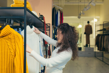 Playful attractive Female customer chooses new clothes, admiring herself in front of a mirror in a stylish boutique of shopping mall