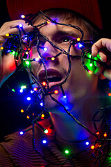 Young guy with a garland. Christmas garland. The guy is holding a garland in front of him, a Christmas decoration. The light of the New Year's lights.