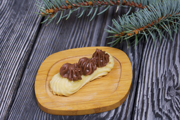Eclairs with chocolate cream. Nearby is a spruce branch. On pine boards.