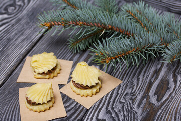 Eclairs with chocolate cream. Nearby is a spruce branch. On pine boards.