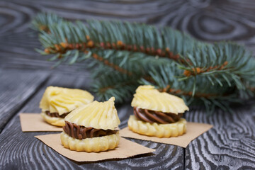 Eclairs with chocolate cream. Nearby is a spruce branch. On pine boards.