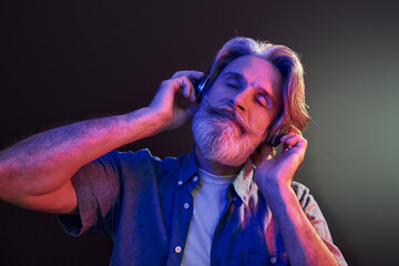 Neon lighting. In headphones. Stylish modern senior man with gray hair and beard is indoors