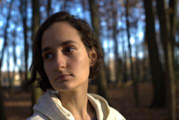 Mujer blanca joven parada en medio del bosque mirando triste a la nada