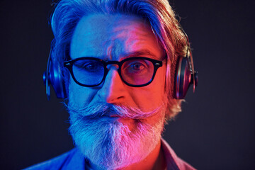 Close up portrait. Neon lighting. Stylish modern senior man with gray hair and beard is indoors