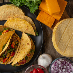 Macro shot view of tasty mexican tacos on rustic wooden table with ingredients for cooking background. Concept of traditional meal. Cookbook illustration. View from above.