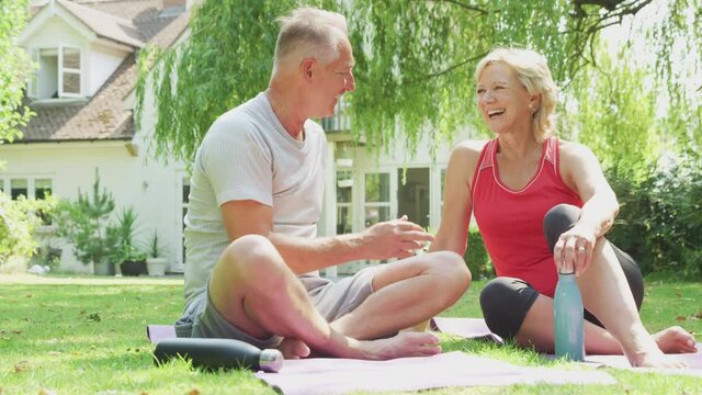 Senior couple at home in garden wearing fitness clothing relaxing and chatting after outdoor yoga class - shot in slow motion