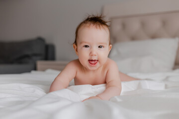 Toddler boy 4 months lies on the bed with a white sheet, space for text