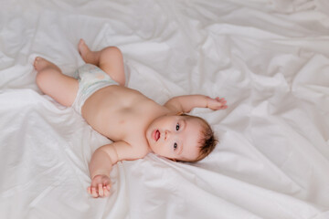 Toddler boy 4 months lies on the bed with a white sheet, the view from above. space for text.