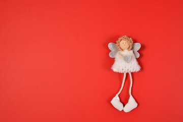 A white angel with silver wings, a heart in his hand and curly Golden hair lies on a red background. A beautiful angel girl holds a heart in her hands and smiles