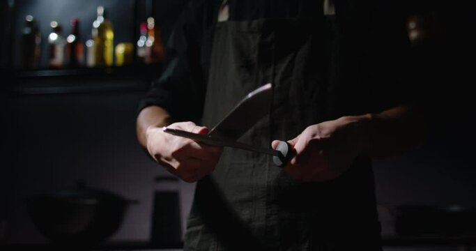 Professional chef is sharpening his knife before cooking a meal. Cool cooker is preparing his tools - food cooking concept close up 4k footage