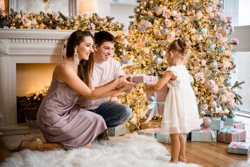 young man and woman give gift to little girl near the christmas tree