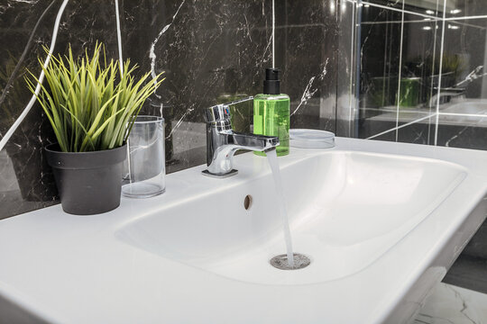 Close up a beautiful snow-white sink with soap, an artificial flower and glassware in a matte bathroom
