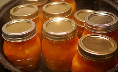 Close-up of of glass jars full of homemade fruit ketchup being sterilized in boiling water
