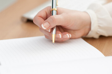 Close-up shot of a woman's hand writing her schedule on the notebook