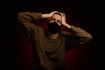 A young guy in a black mask is holding his head. Pandemic. Self-isolation. 