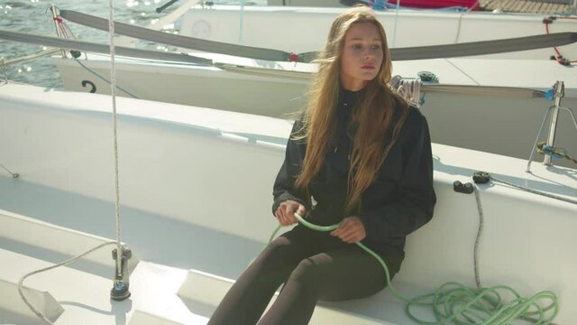 A female athlete checks the rigging while sitting on board a white yacht before traveling down the river on an autumn day