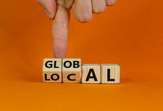 Local or global symbol. Hand turns cubes and changes the word 'local' to 'global'. Beautiful orange background. Business and local or global concept. Copy space.