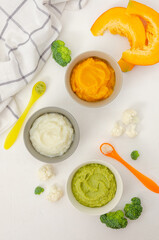 Baby food. Variation of the three homemade vegetable puree in bowls. Pumpkin puree, cauliflower puree and broccoli puree on a white background. Top view.