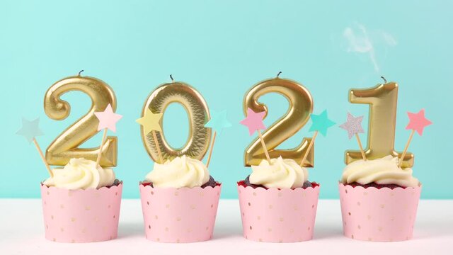 2021 Happy New Year's Eve pastel pink and blue theme cupcakes with large gold candles. Blowing out candles.