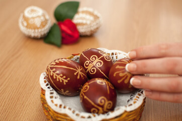 Woman hands arranging dyed traditional easter eggs with handmade patterns in paper basket