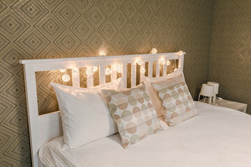 Close up soft white beautiful bed with beautiful square pillows and lamps standing in a room with green wallpaper