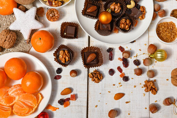 sweet food background for christmas or holiday decoration - chocolate candies, tangerines, nuts and dried fruits on white wood