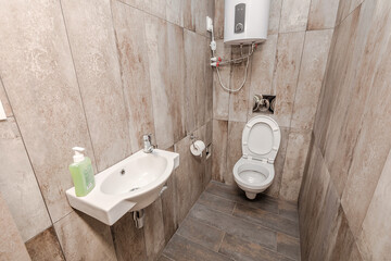 Cozy bathroom with light-tiled walls in which there is a white ceramic sink, toilet and boiler