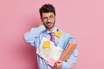 Tired exhausted employee has neckpain holds folders and wears shirt with attached sticky notes written information poses against pink background. Fatigue student studies hard before final exam