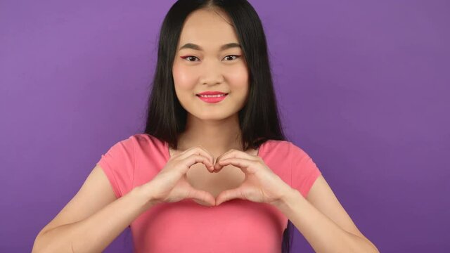 close-up portrait of woman showing heart gesture. Isolated young Asian woman on purple background. 4K