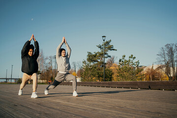 a strong pair of male and female African-American. cardio fitness aerobics workout on the waterfront in the city Park. do active stretching fitness exercises on the street.