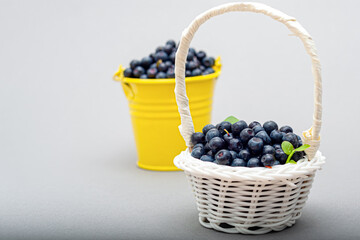 yellow bucket and wicker white basket of ripe blueberry with green leaf on white background