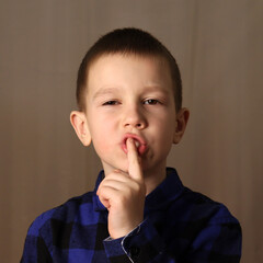a child in a blue shirt holds a finger to his mouth