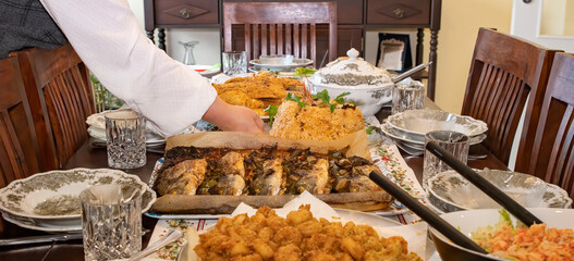 A woman's hand places a plate of rice on the dinner table with the fish dishes.