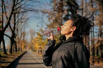 a woman drinks clean, healthy cold water during a morning jog in the city's Central Park. sports fitness an African-American woman is engaged in a healthy lifestyle. sportive